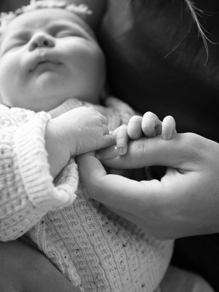 Mama hält die zarten Händchen ihres Neugeborenen