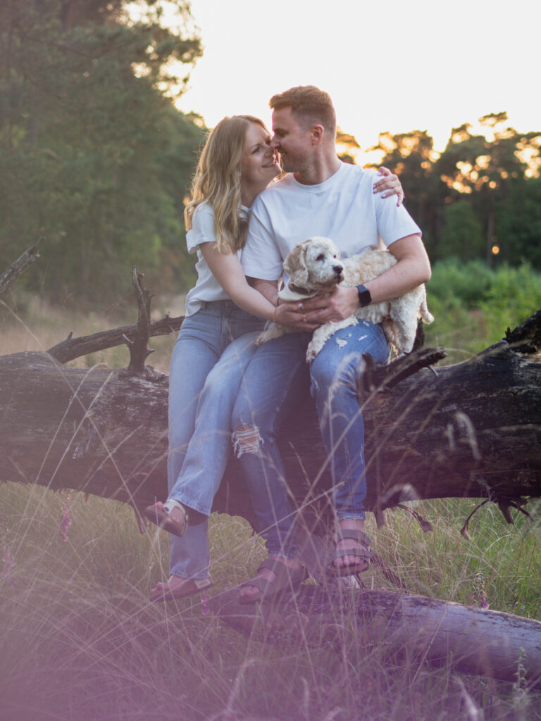 Pärchen sitzt auf einem Baumstamm mit Hund auf dem Schoß