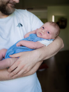 Baby in blauem Strampler auf Papas Arm